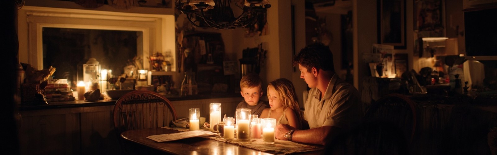 Father and children gathered around candles at kitchen table during hurricane power outage