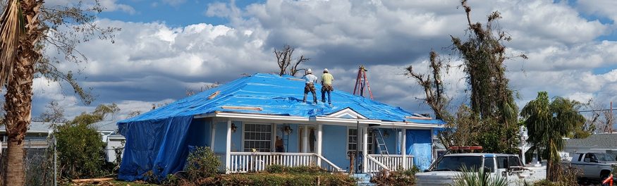 Workers installing blue FEMA tarp on hurricane damaged roof