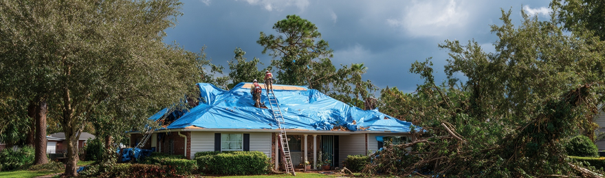 Workers tarping brick home roof after hurricane